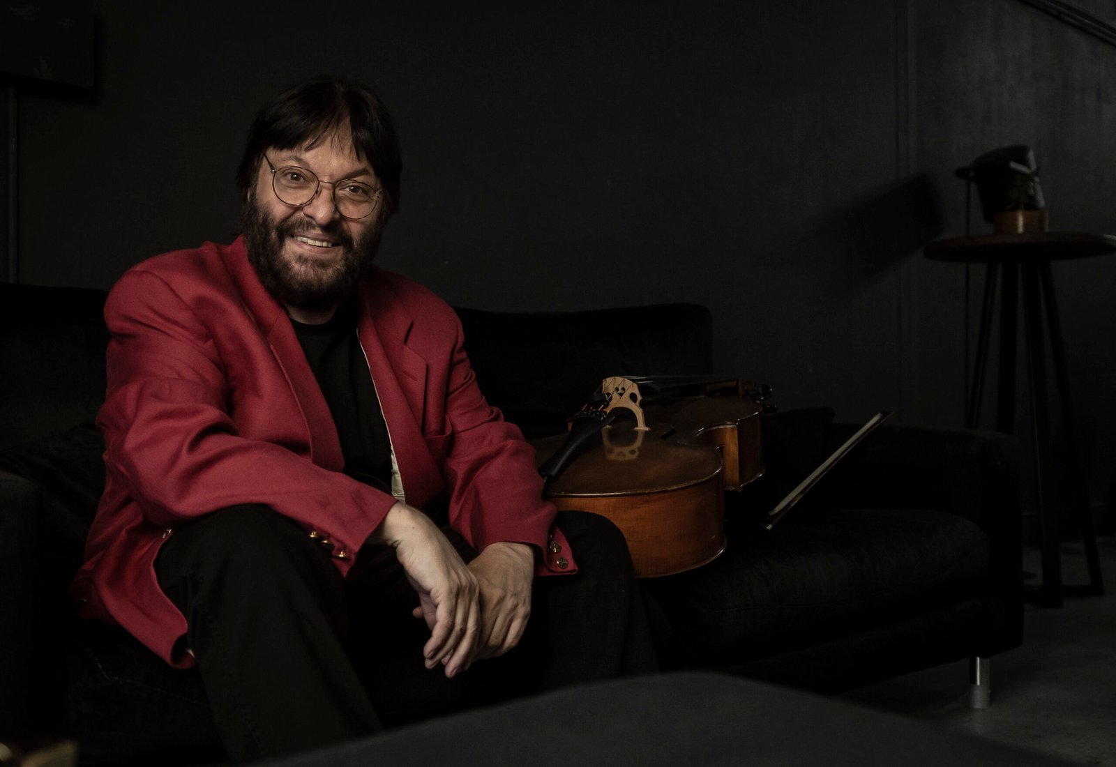 Patricio Villarejo sonriendo en un sillón, con el violonchelo al lado